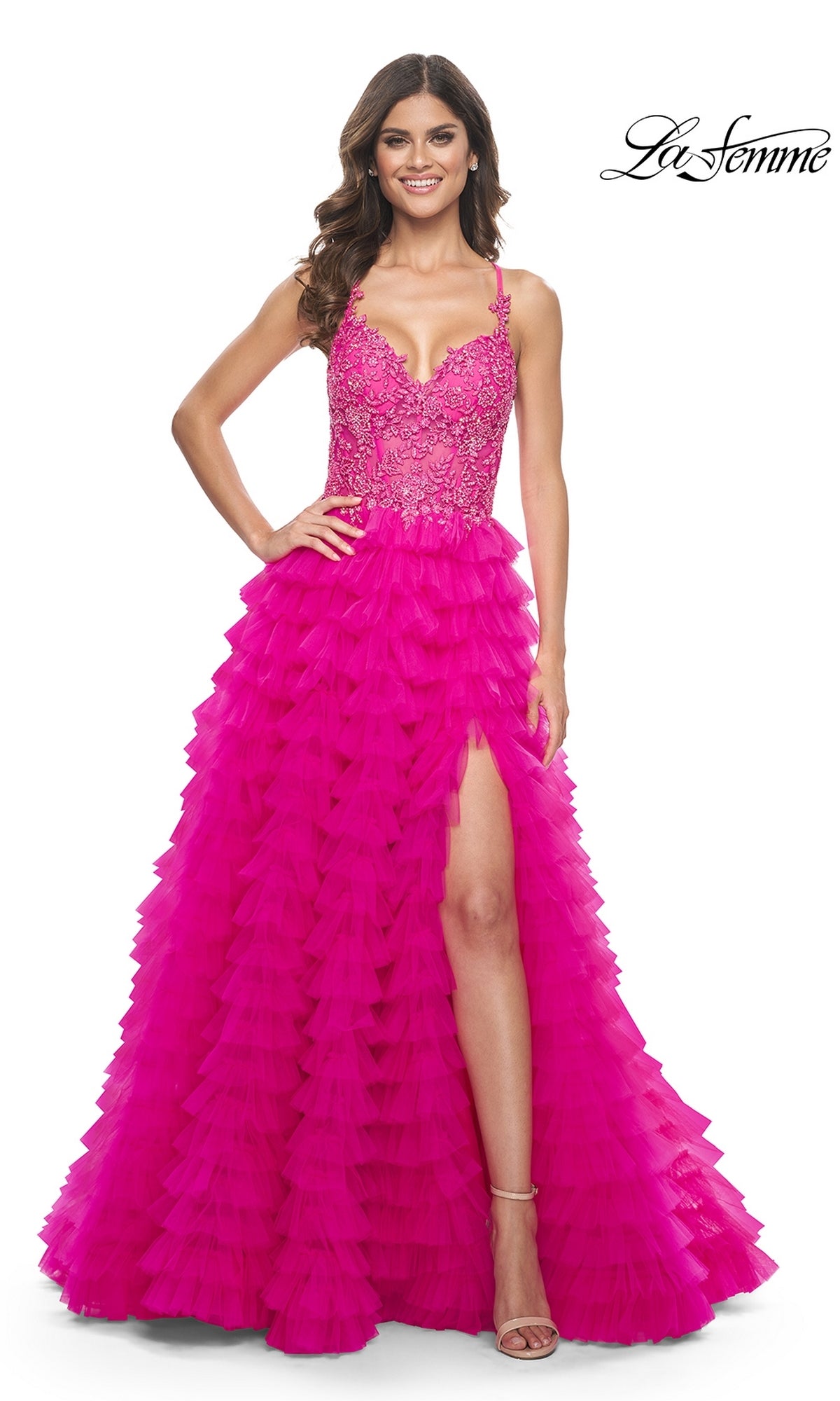 A woman stands smiling in the La Femme Hot Pink Long Ruffled Prom Dress 32334, featuring an embroidered-lace bodice, thin straps, and a high-slit ruffled A-line skirt.